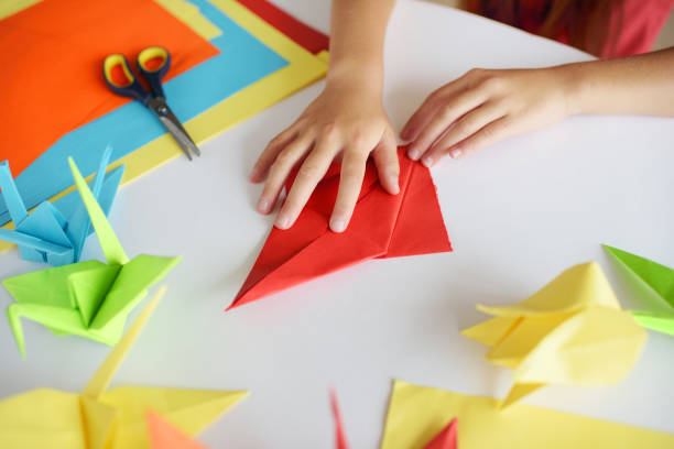 Children's hands do origami from colored paper on white background.