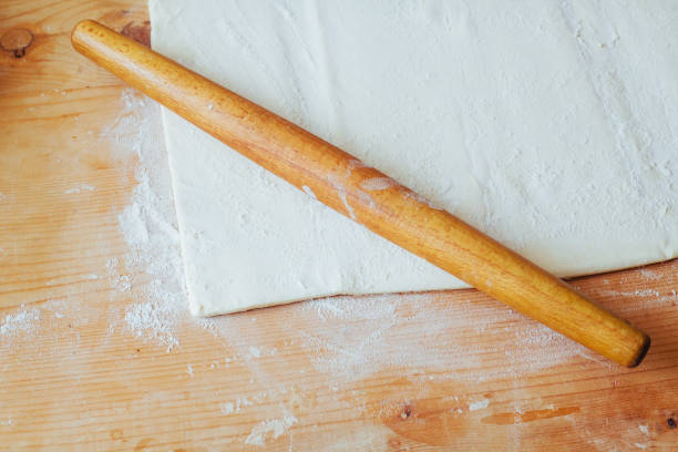 istock Block of freshly made pastry rolled out on a floured work surface with a wooden rolling pin 844038574