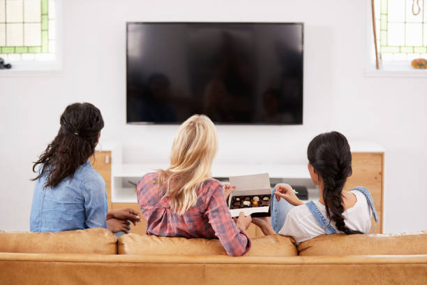 istock Female Friends Sitting On Sofa Watching Television Eating Candy 844053422