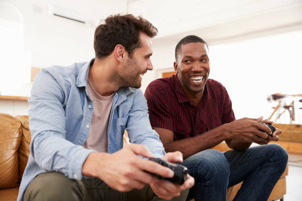 istock Two Male Friends Sitting On Sofa In Lounge Playing Video Game 844054154