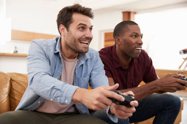 istock Two Male Friends Sitting On Sofa In Lounge Playing Video Game 844054224