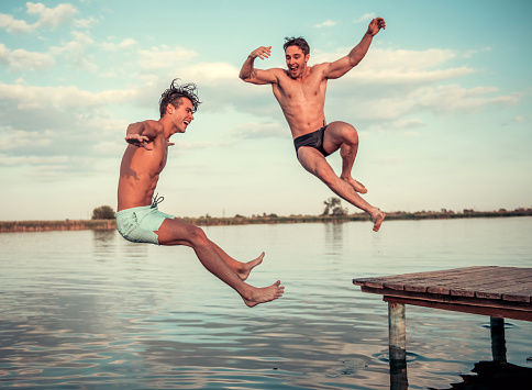 Handsome guys are jumping from pier into the lake, beautiful view