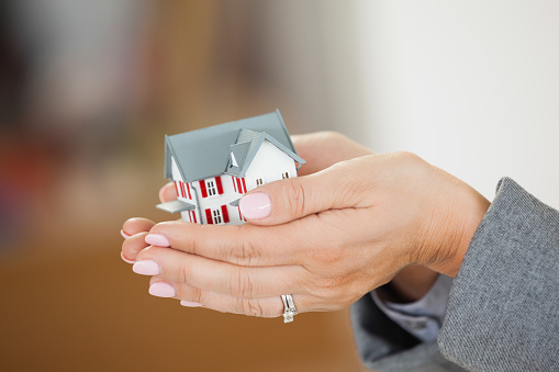 Woman holding a tiny house in her hands with a blurred background