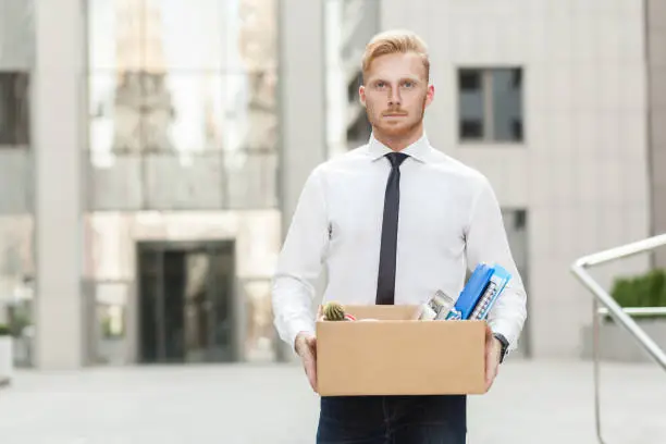 Youre fired. Unhappy bearded business man going out with cardboard, looking at camera and feeling looser. Outdoor