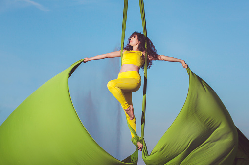 Athlete aerial acrobatics on a hammock, she stands high in the sky.