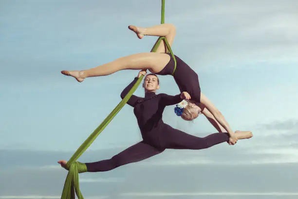Two women aerial gymnasts perform high in the sky on hammocks.