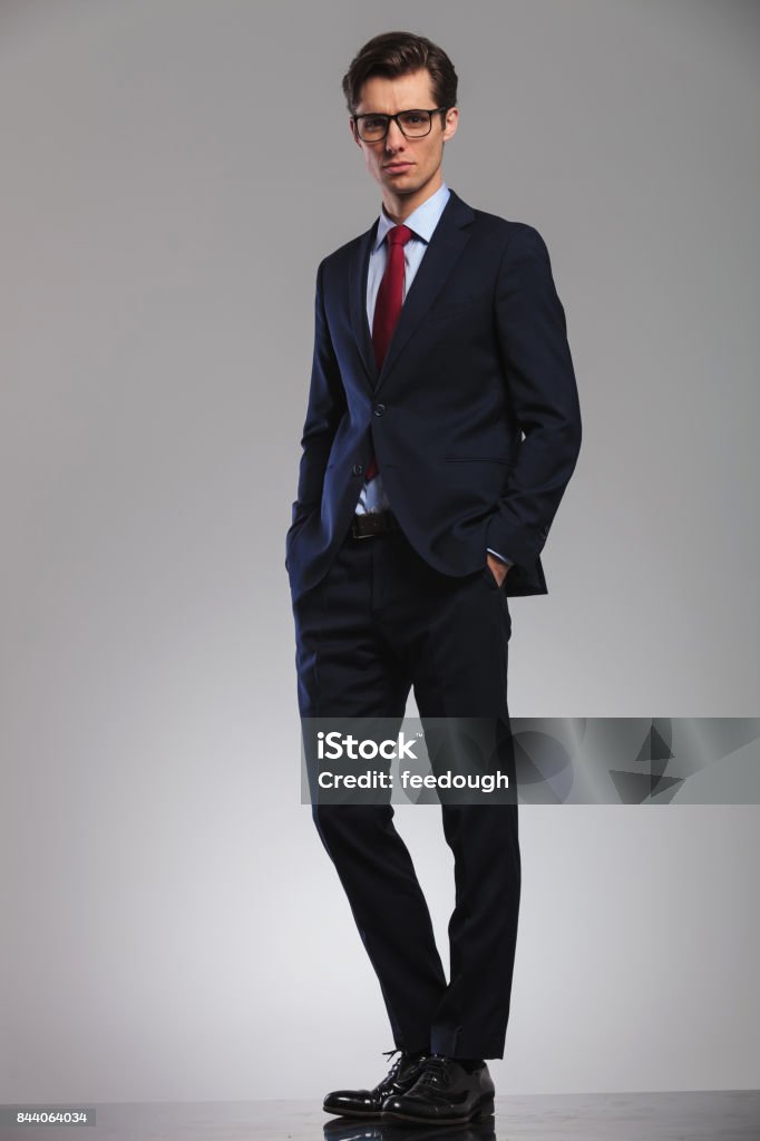 young business man standing with hands in pockets full body picture of a young business man standing with hands in pockets on grey studio background Suit Stock Photo