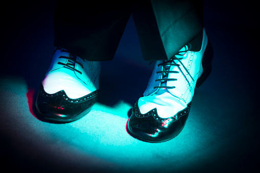 Male latin and salsa dancer in black and white jazz dancing shoes in light and dark on stage.