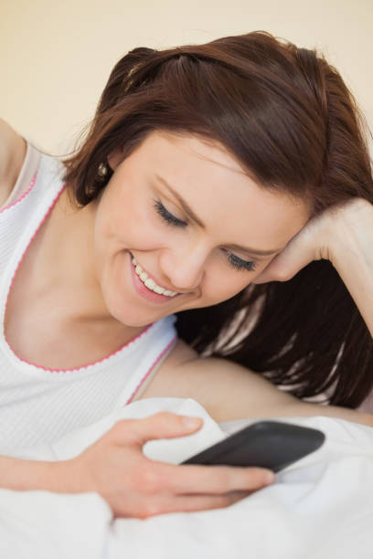 istock Cheerful girl using a mobile phone lying on a bed 844133460