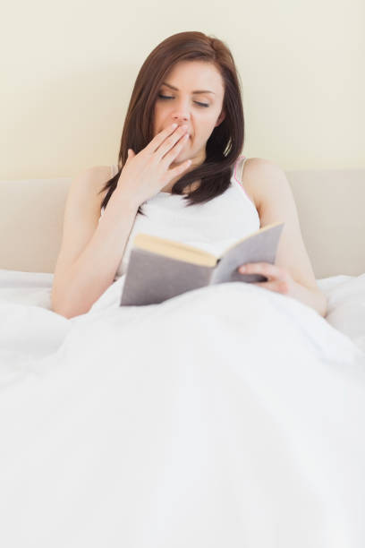 istock Yawning girl reading a book lying on a bed 844136342