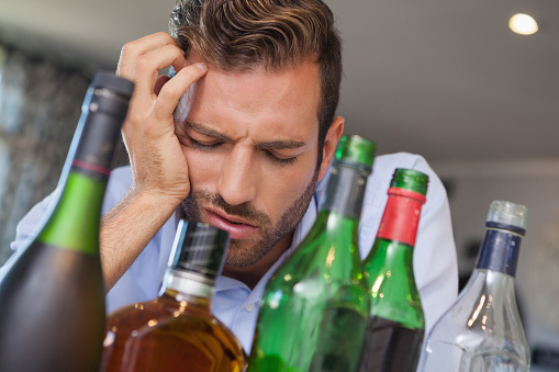 Drunk businessman slumped beside many spirit bottles at the local bar