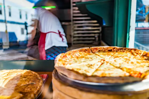 Photo of Closeup of fresh handmade pizza in store bakery on display by window with chef employee working