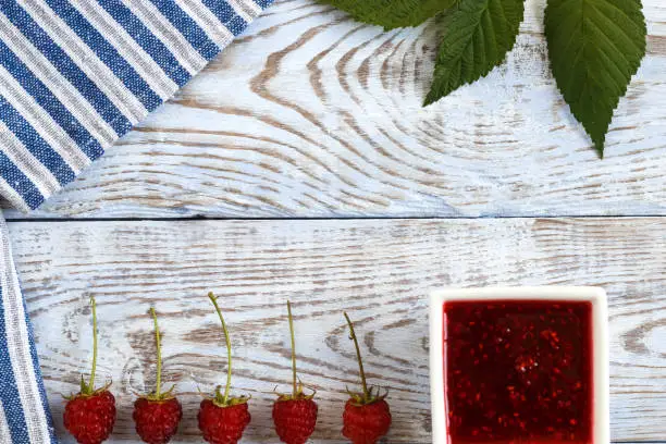 Fresh raspberry and raspberry jam on a wooden background. Berries lie in a row