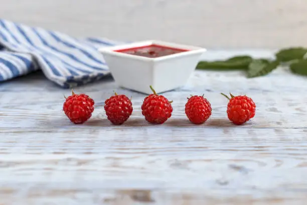 Fresh raspberry and raspberry jam on a wooden background. Berries lie in a row. Copy space