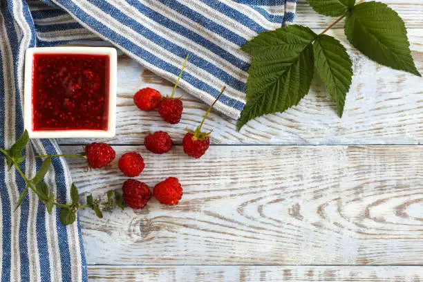 Fresh raspberry and raspberry jam on a light wooden background. Copy space