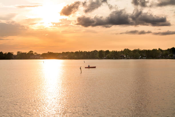 A young man is paddling a Canadian Algonquin prospector canoe on a lake, against sunset background.