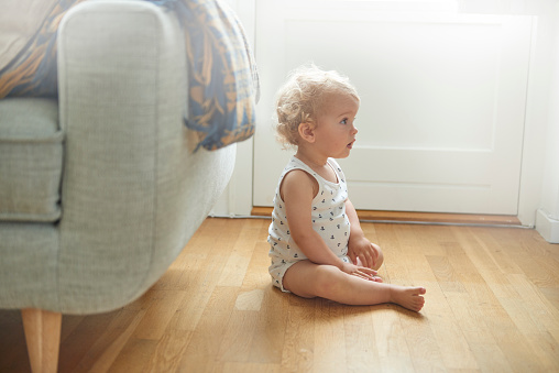 Small child is sitting on the floor profile view. Light from the window behind is causing some lens flare. Bright pastel color