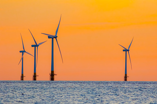 Offshore wind farm energy turbines at dawn. Surreal but natural sunrise at sea. Modernistic image. The future of clean energy production.