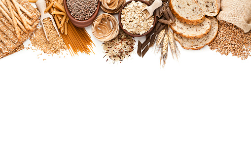 Top view view of wholegrain and cereal food placed at the top border of an horizontal white background making a frame and leaving useful copy space for text and/or logo. This type of food is rich of fiber and is ideal for dieting. The composition includes wholegrain sliced bread, wholegrain pasta, oat flakes, flax seed, brown rice, brown lentils, wholegrain crackers, breadsticks and spelt. Predominant colors are brown and white. DSRL studio photo taken with Canon EOS 5D Mk II and Canon EF 100mm f/2.8L Macro IS USM