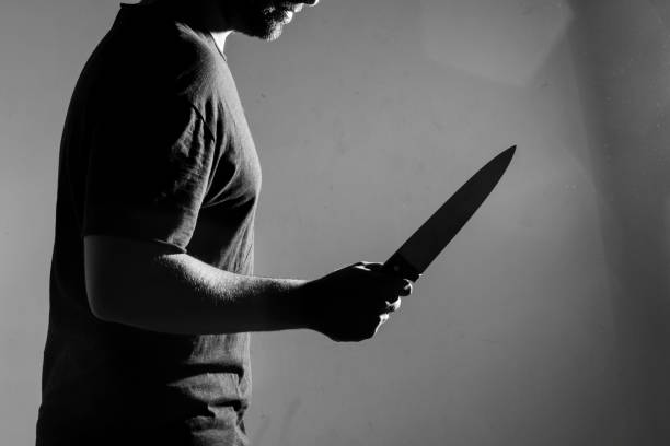 Man in black t-shirt, standing holding a knife. Man in black t-shirt, standing holding a knife. Indoors. Converted to black and white, grain added. serial killings photos stock pictures, royalty-free photos & images