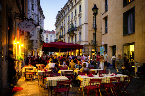 Turin, Italy - June 18, 2017: The Quadrilatero, night life and restaurant district of Turin (Italy) at evening, on june 18, 2017, with people sitting at the tables, eating and walking