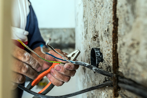 Photo of Electrician peeling off insulation from wires - closeup on hands and pliers. electrician binding copper wires together and sealing them with insulation stripe. Man mounting the wires into electrical wall fixture or socket - closeup on hands and pliers.