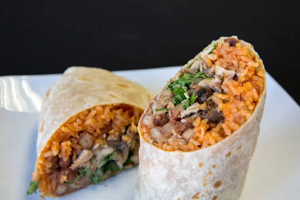 Tow halves of a burrito with rice, beans, and steak on a white plate