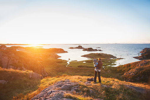 Rear view of a woman mother dressed in outdoor clothing holding her toddler son boy looking out at a spectacular sunset on the Ilse of Mull Highlands Scotland United Kingdom UK