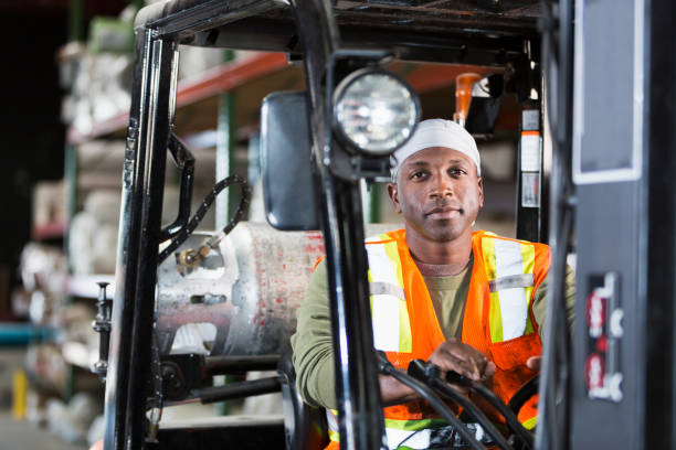 Man operating forklift in carpet warehouse An African-American man in his 30s wearing a safety vest operating a forklift in a carpet warehouse. He is looking at the camera with a serious expression. do rag stock pictures, royalty-free photos & images