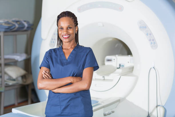 Technician standing in front of MRI scanner A successful, mature black woman working as a medical professional in a hospital or clinic, standing in front of an MRI scanner, smiling at the camera. mri scanner photos stock pictures, royalty-free photos & images