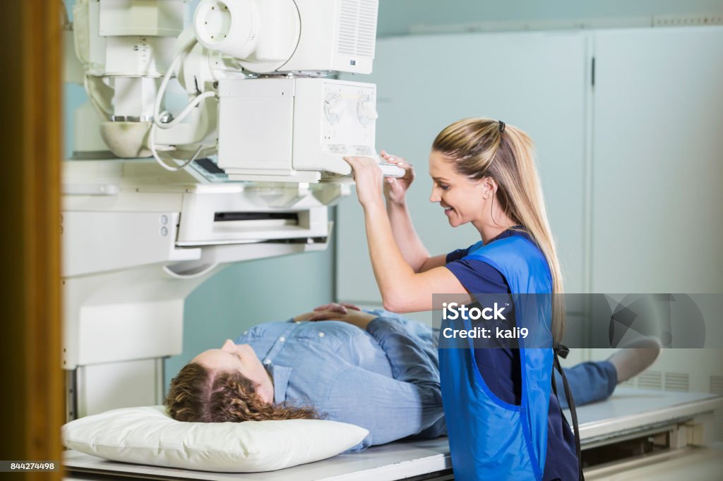 Technician with patient getting x-ray A medical professional with a female patient who is lying on her back getting an x-ray. Technician Stock Photo