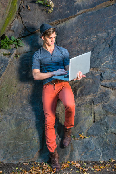 Young Man Working on laptop computer outside by rocks