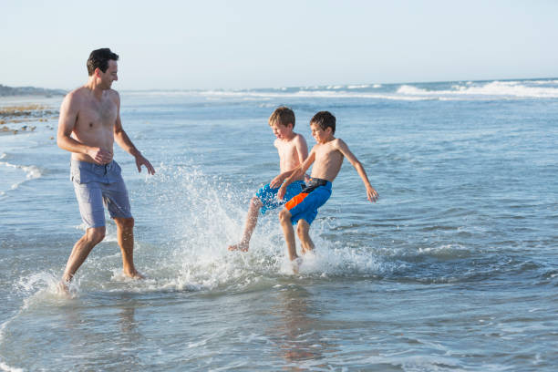 istock Father and two sons playing in water at beach 844297138