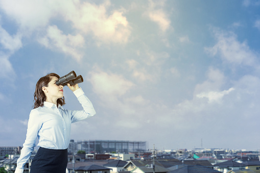 young woman holding binocular glasses. residential houses background.