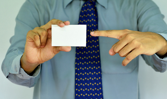 Hand of a businessman with a blank card on a gray background.