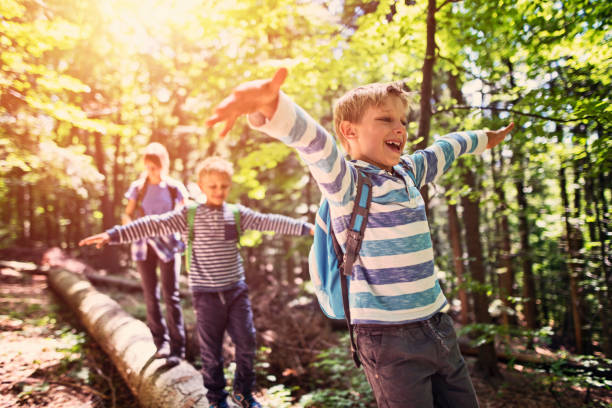 Little hikers walking on a tree trunk  in forest Happy kids hiking in a forest. Children are walking on a faller tree trunk, balancing with arms outstretched.

 eco tourism photos stock pictures, royalty-free photos & images