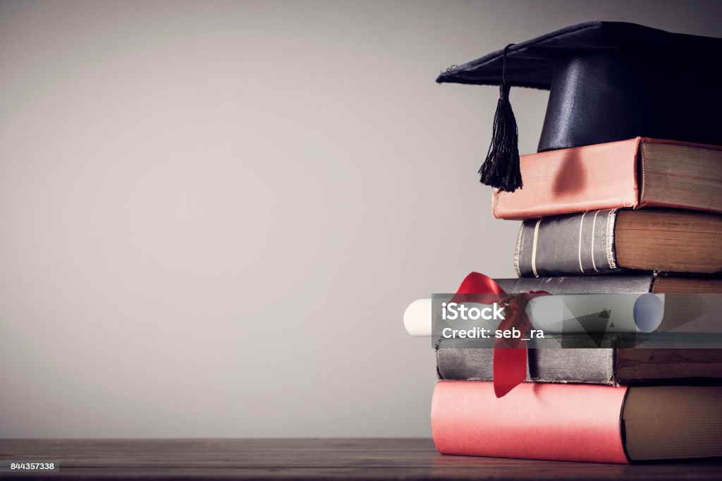 Graduation hat and diploma with book on table Post-Secondary Education Stock Photo