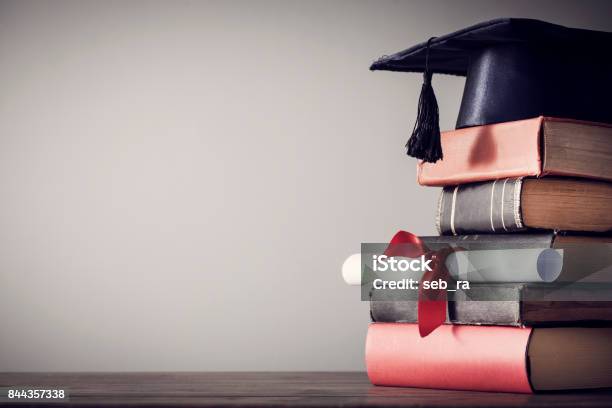 Foto de Chapéu De Formatura E Diploma Com O Livro Na Mesa e mais fotos de stock de Ensino superior - Ensino superior, Formatura, Universidade