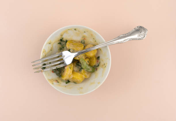 Top view of an almost finished bowl of yellow carrots and green beans in a parmesan cheese sauce with a fork atop a pink stone table top.