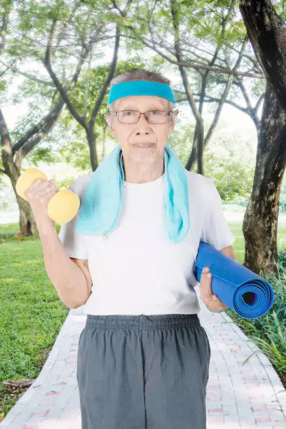 Portrait of elderly man holding a dumbbell and mat while walking in the park