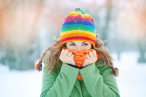 Portrait of a young woman in snow with scarf on her face trying to warm herself. Winter concept