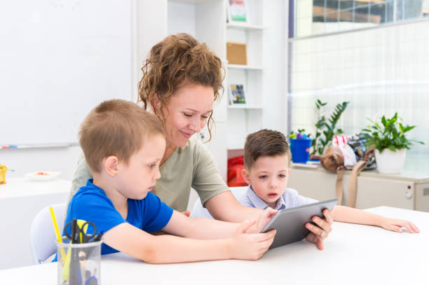 istock teacher woman using tablet computer with two preschooler boy in a classroom 844385924