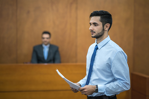 Portrait of a young lawyer holding documents in the courtroom - legal system concepts