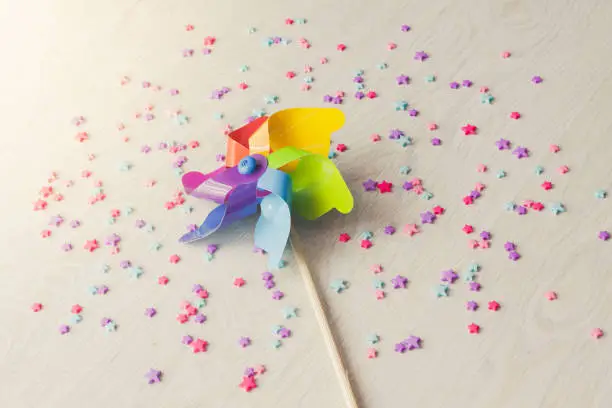 Photo of Colorful paper windmill pinwheel on white floor many plastic stars below