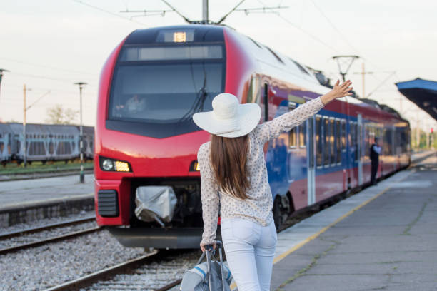 A happy young traveler woman with luggage standing in train door waveing out of train at train station platform