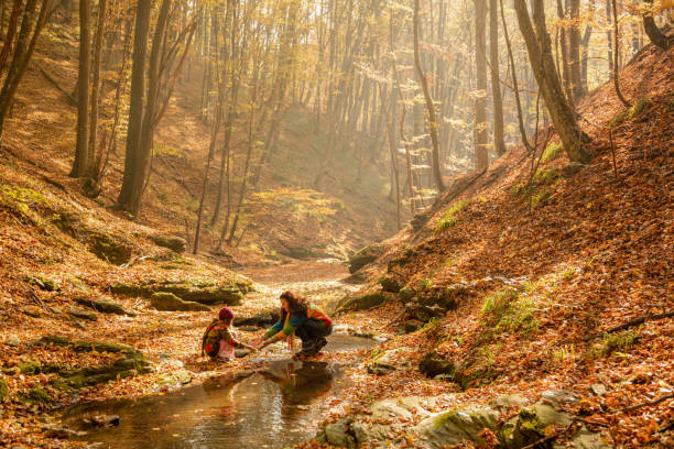 Mother playing with her daughter by the river while hiking in beautiful forest at autumn