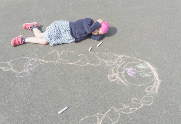 Boy at home, sheltering in place occupying time by drawing on sidewalk with chalk.