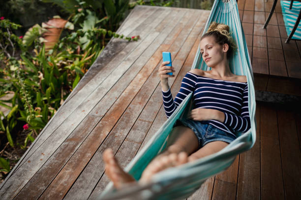 Ready to Relax Young woman lying down on a hammock, using her smartphone and relaxing. hammock relaxation women front or back yard stock pictures, royalty-free photos & images