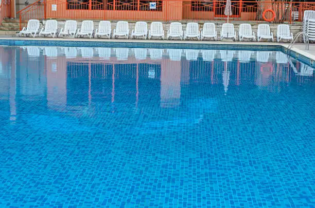 Photo of Blue water swimming pool with white plastic sunbeds