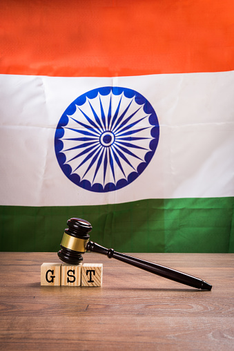 Stock photo of GST low in india. GST text  written over wooden blocks with wooden gavel over it and indian national flag or tricolour in the background, selective focus